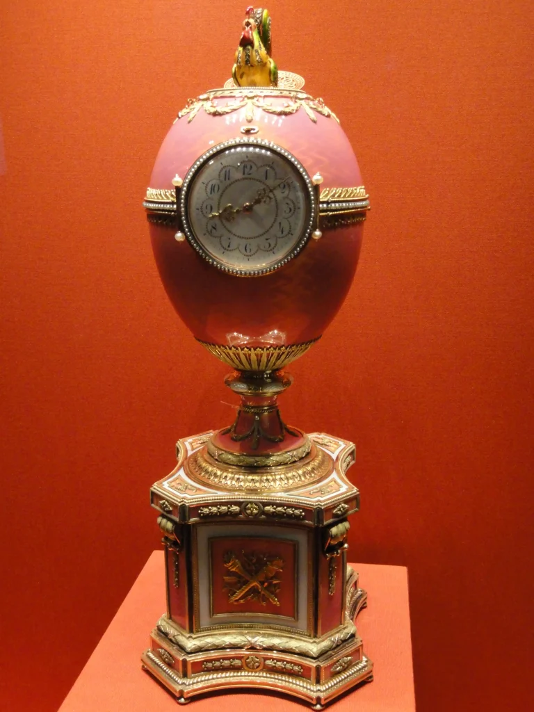 Huevo de Fabergé Rothschild de 1902 con reloj frontal y gallo mecánico autómata sobre fondo rojo