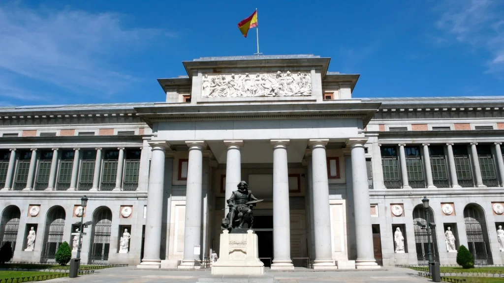 Fachada principal del Museo Nacional del Prado en Madrid con columnas y estatua frente al edificio.