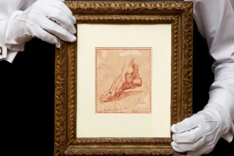 Manos con guantes sosteniendo dibujo enmarcado de estudio anatómico atribuido a Michelangelo relacionado con la Capilla Sixtina