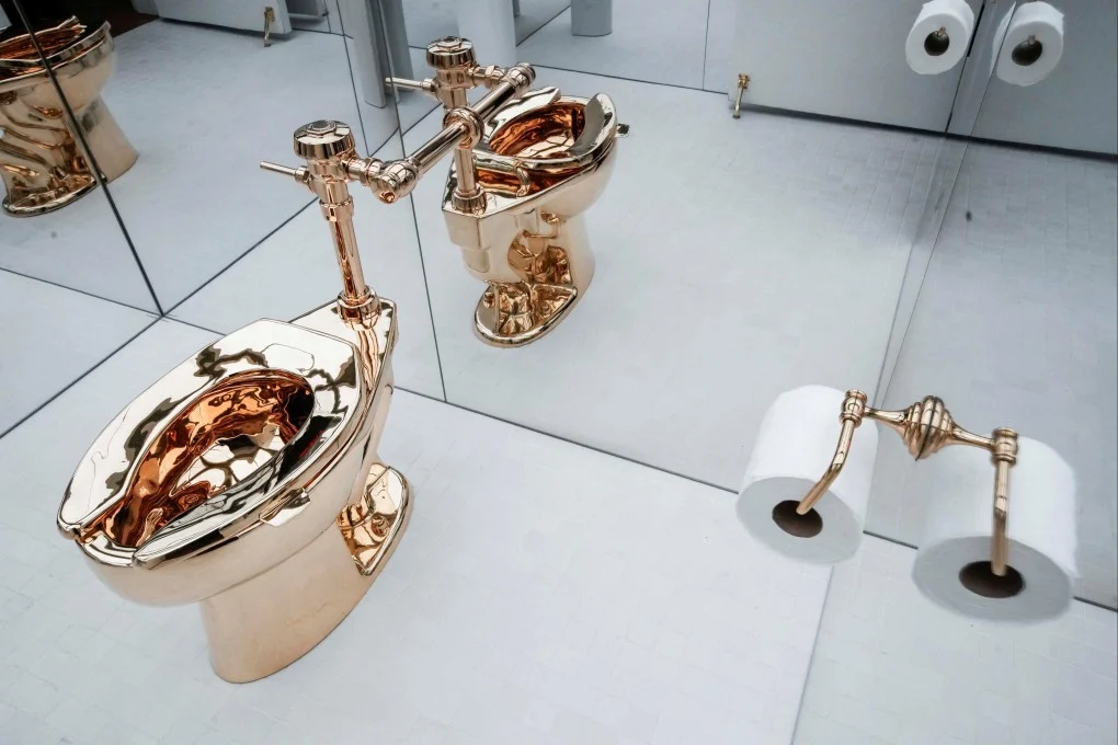 La obra America de Maurizio Cattelan, un inodoro funcional fabricado en oro de 18 quilates, exhibido en una sala con paredes de espejo.