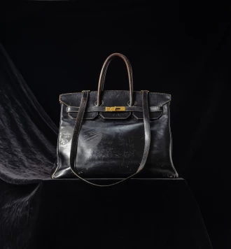 Bolso original de Jane Birkin de cuero negro exhibido sobre un pedestal oscuro, pieza histórica que estableció el récord mundial como el bolso más caro vendido en una subasta pública.