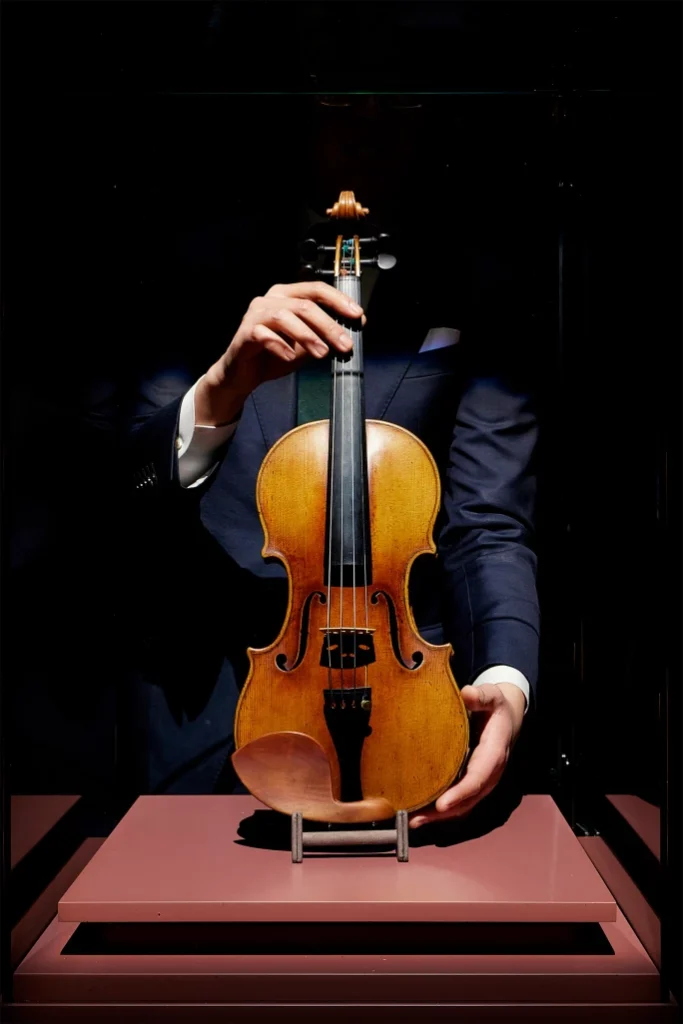 Violín histórico inspirado en el Stradivarius "Joachim-Ma" sostenido por una persona durante una exhibición en un entorno con iluminación tenue.