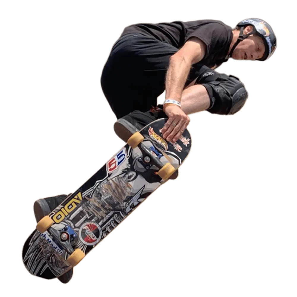Tony Hawk realizando un salto en el aire sobre su patineta, utilizando casco y rodilleras durante una maniobra de skateboarding.